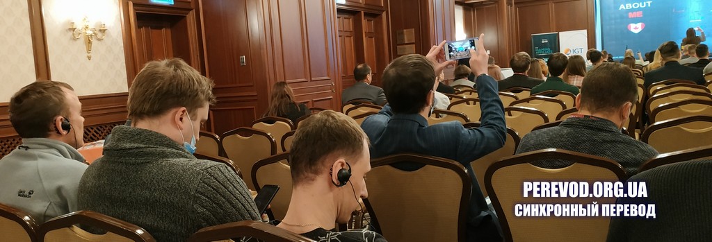 Участники конференции с наушниками для синхронного перевода слушают англоязычного спикера на русском языке.